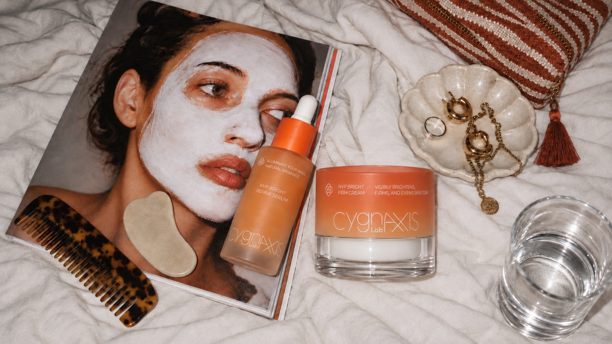CYGNAXIS Lab serum and face cream arranged on a bed beside a magazine and personal objects.