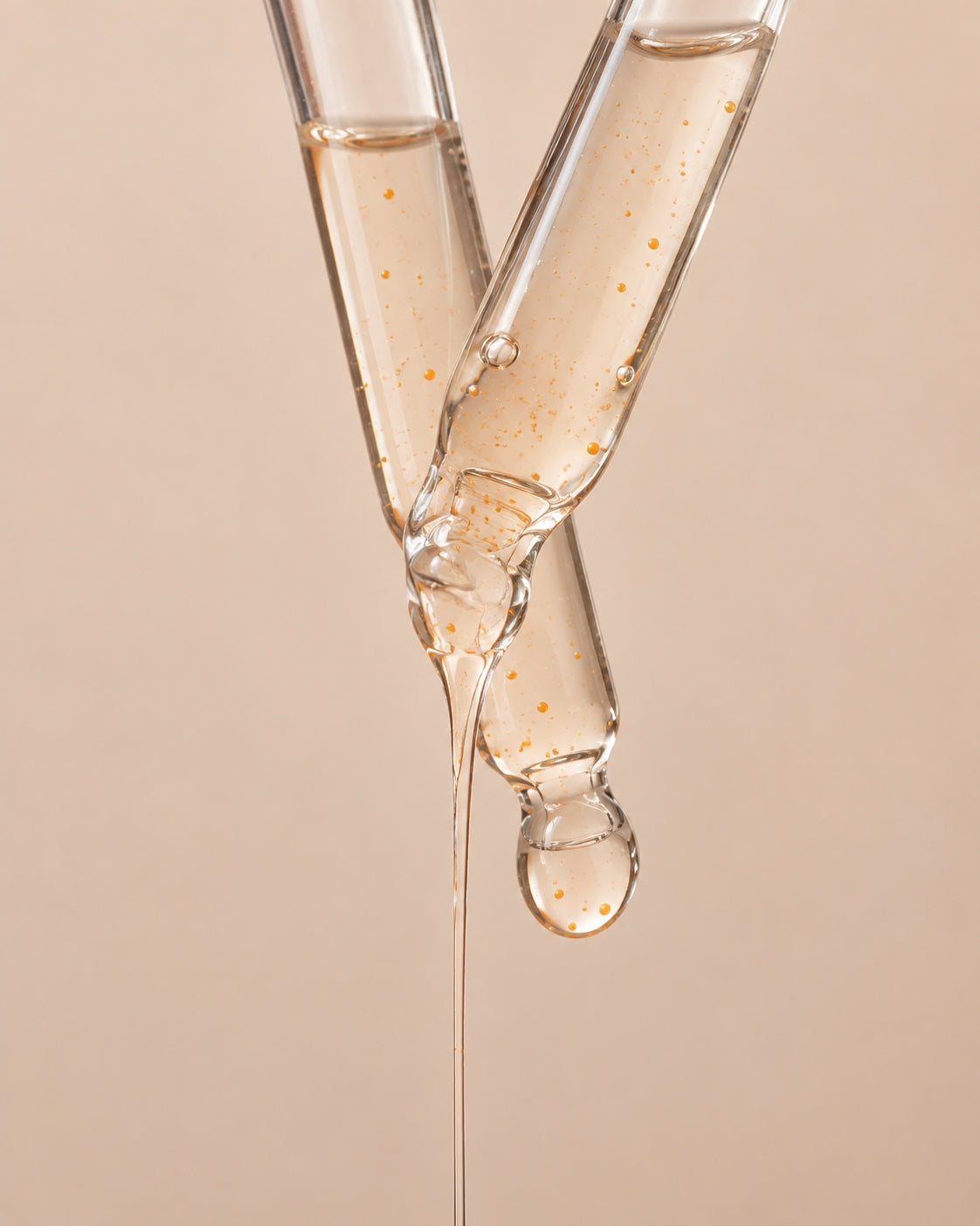 Close-up of translucent serum flowing between glass droppers with visible orange microbeads.